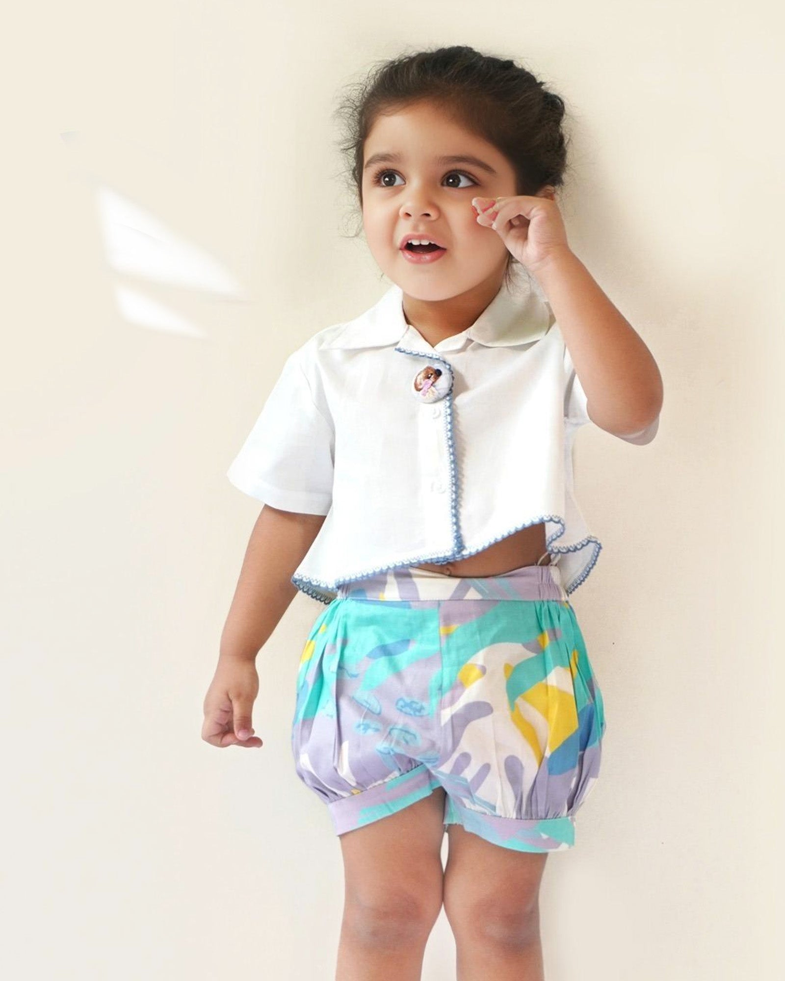 baby girl wearing  Laad`s gwhite cropped shirt with scalloped trim and hand-embroidered button on it along with pastel aqua bubble shots featuring a pleated abstract design.