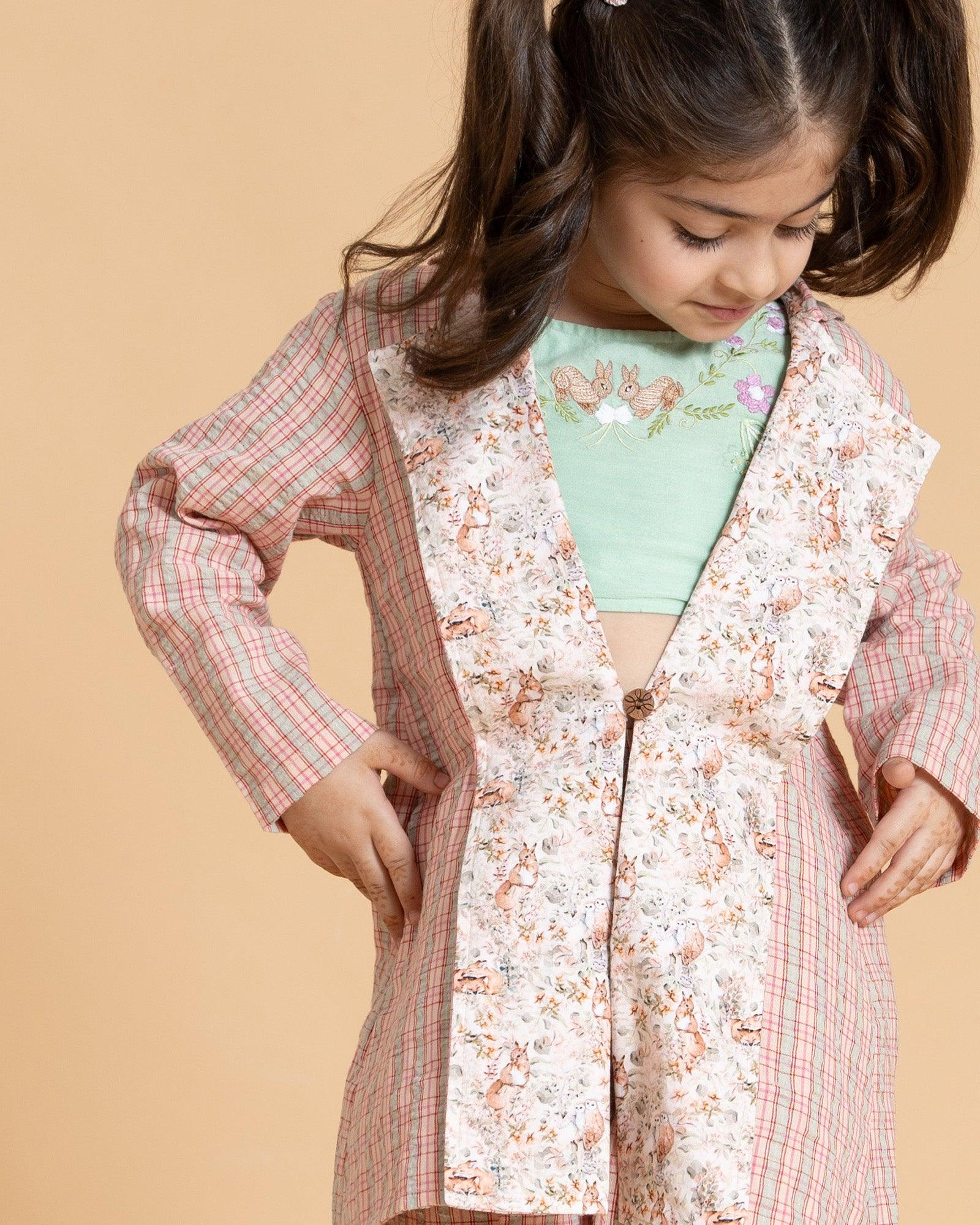 A vibrant Blooming Meadow Co-ord Set featuring a sleeveless silk Chanderi crop top with playful bunny embroidery and intricate threadwork, paired with a long coat featuring a meadow-inspired printed collar. Complete with breezy culottes pants that offer a stylish yet comfortable kidswear fit.