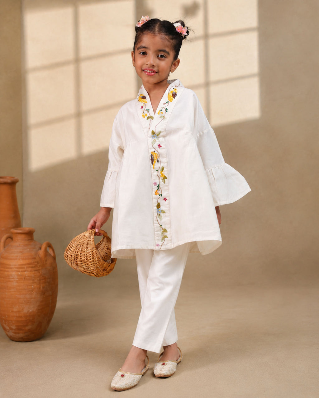 A young girl modeling a white kimono  flower look co-ord   set with colorful floral bird embroidery down the front placket by laandindia.com