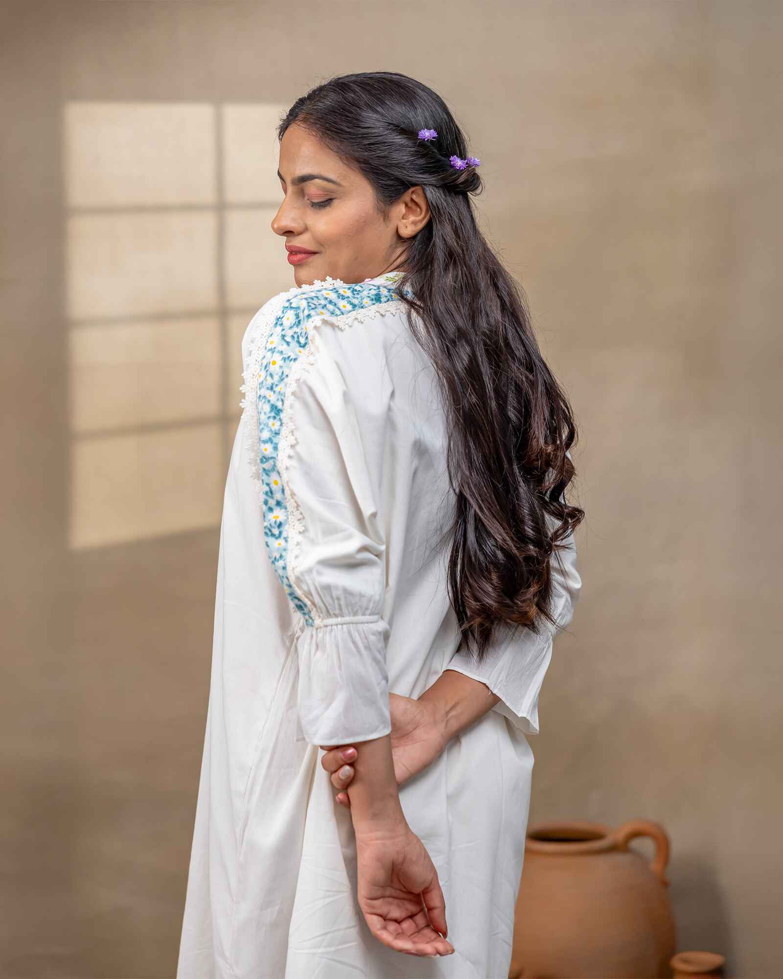 Model wearing a white laad`s midi cotton dress with pastel floral embroidery on the neckline and blue threadwork on the sleeves, featuring a ruffled hem and relaxed fit.