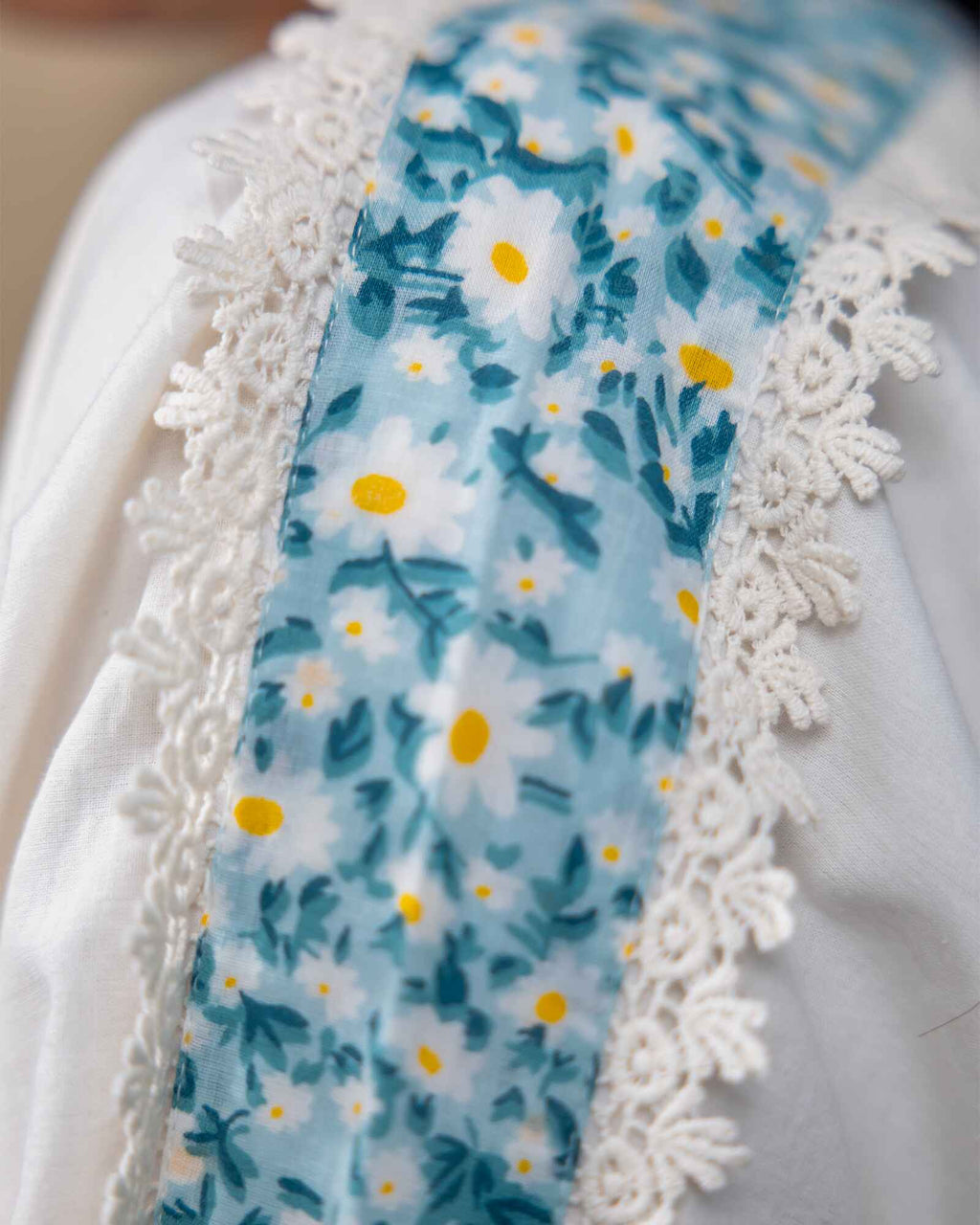 Model wearing a white laad`s midi cotton dress with pastel floral embroidery on the neckline and blue threadwork on the sleeves, featuring a ruffled hem and relaxed fit.