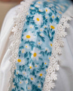 Model wearing a white laad`s midi cotton dress with pastel floral embroidery on the neckline and blue threadwork on the sleeves, featuring a ruffled hem and relaxed fit.