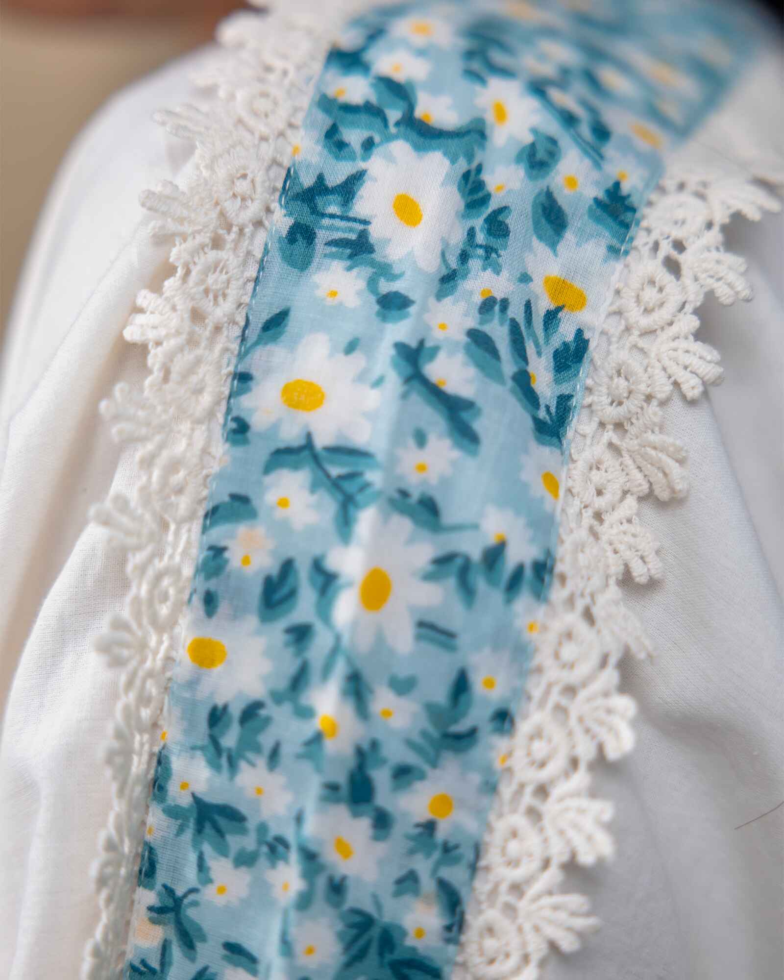 Model wearing a white laad`s midi cotton dress with pastel floral embroidery on the neckline and blue threadwork on the sleeves, featuring a ruffled hem and relaxed fit.