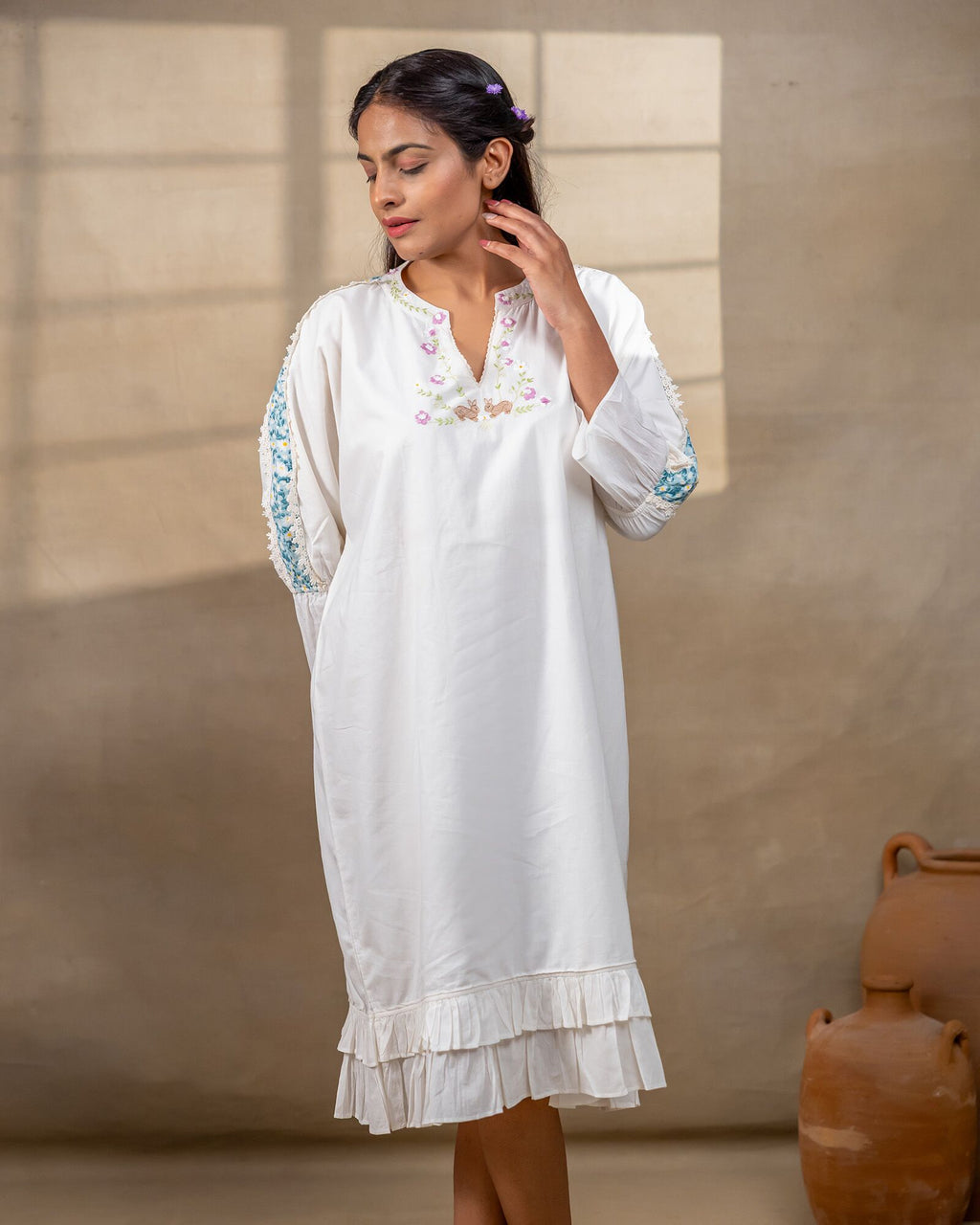 Model wearing a white laad`s midi cotton dress with pastel floral embroidery on the neckline and blue threadwork on the sleeves, featuring a ruffled hem and relaxed fit.