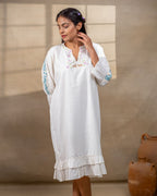 Model wearing a white laad`s midi cotton dress with pastel floral embroidery on the neckline and blue threadwork on the sleeves, featuring a ruffled hem and relaxed fit.