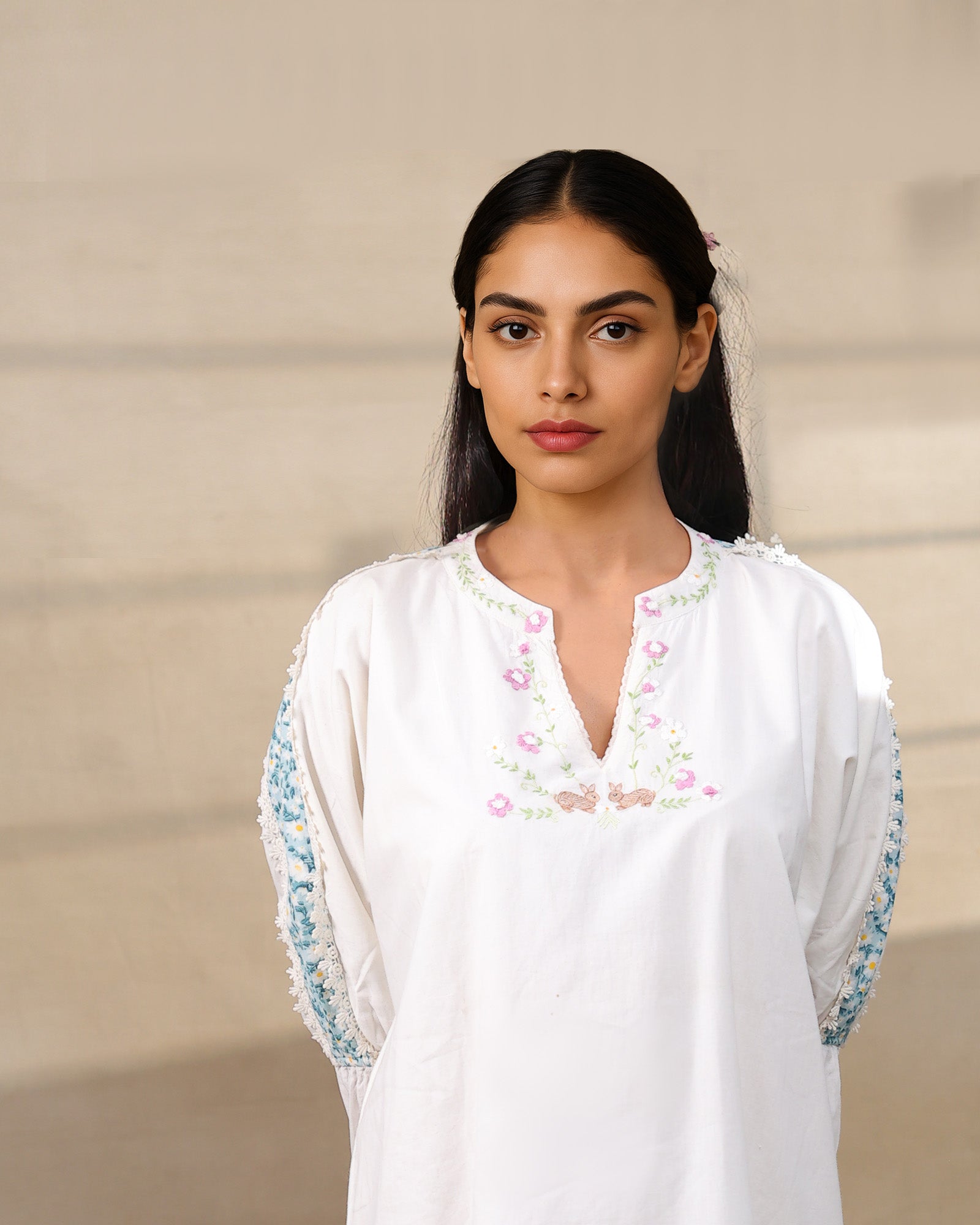 Model wearing a white laad`s midi cotton dress with pastel floral embroidery on the neckline and blue threadwork on the sleeves, featuring a ruffled hem and relaxed fit.