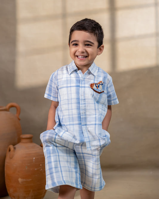 LAAD`S kids in co-ord set featuring a light blue and white plaid short-sleeve button-up shirt with matching shorts. The shirt is adorned with delicate embroidery of a rocking horse on the chest,