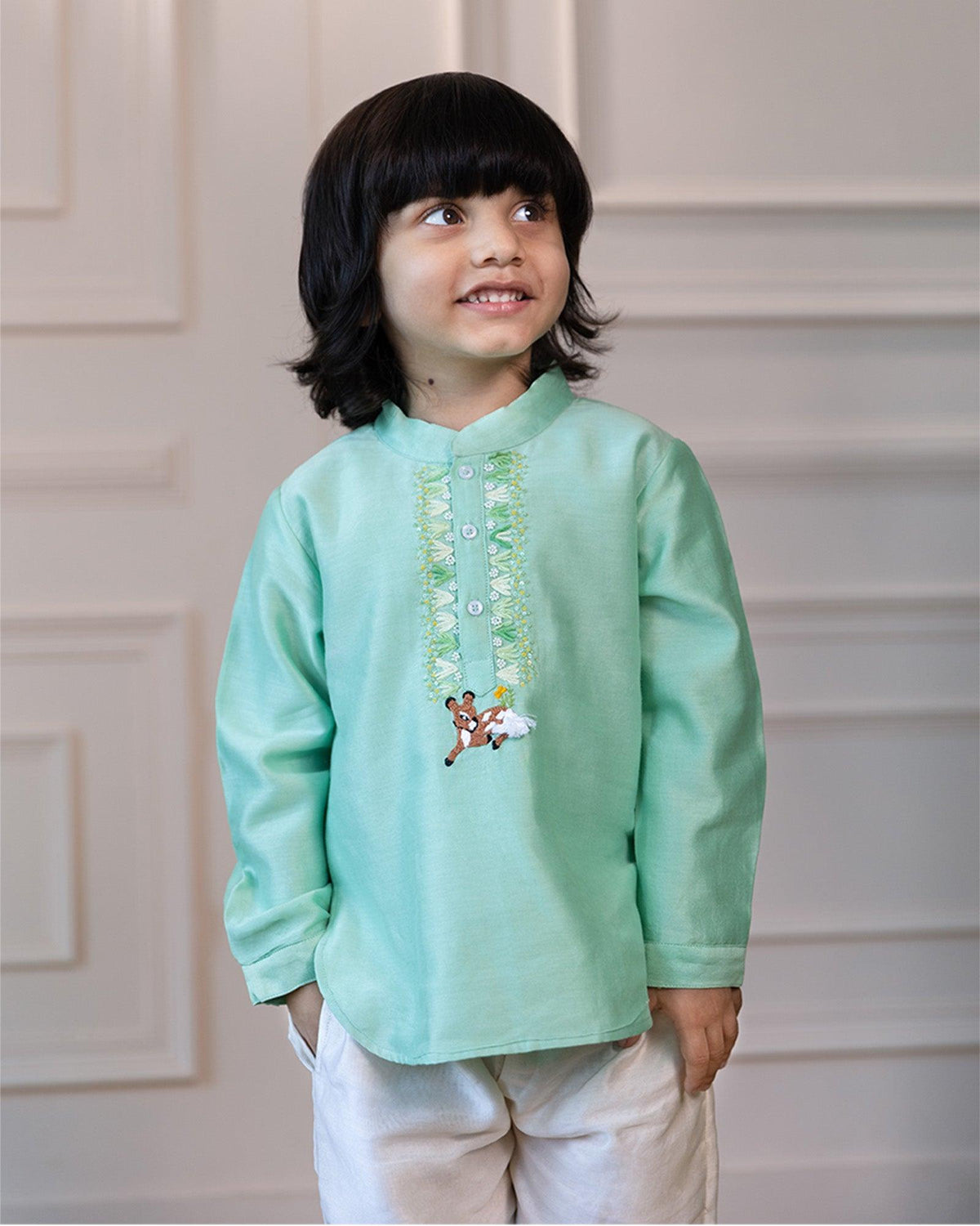 Elevate tradition with this short kurta featuring a bandhgala collar, hand-embroidered ari-work, sequins, and a handcrafted bambi. Paired with ivory pants, perfect for festivities.