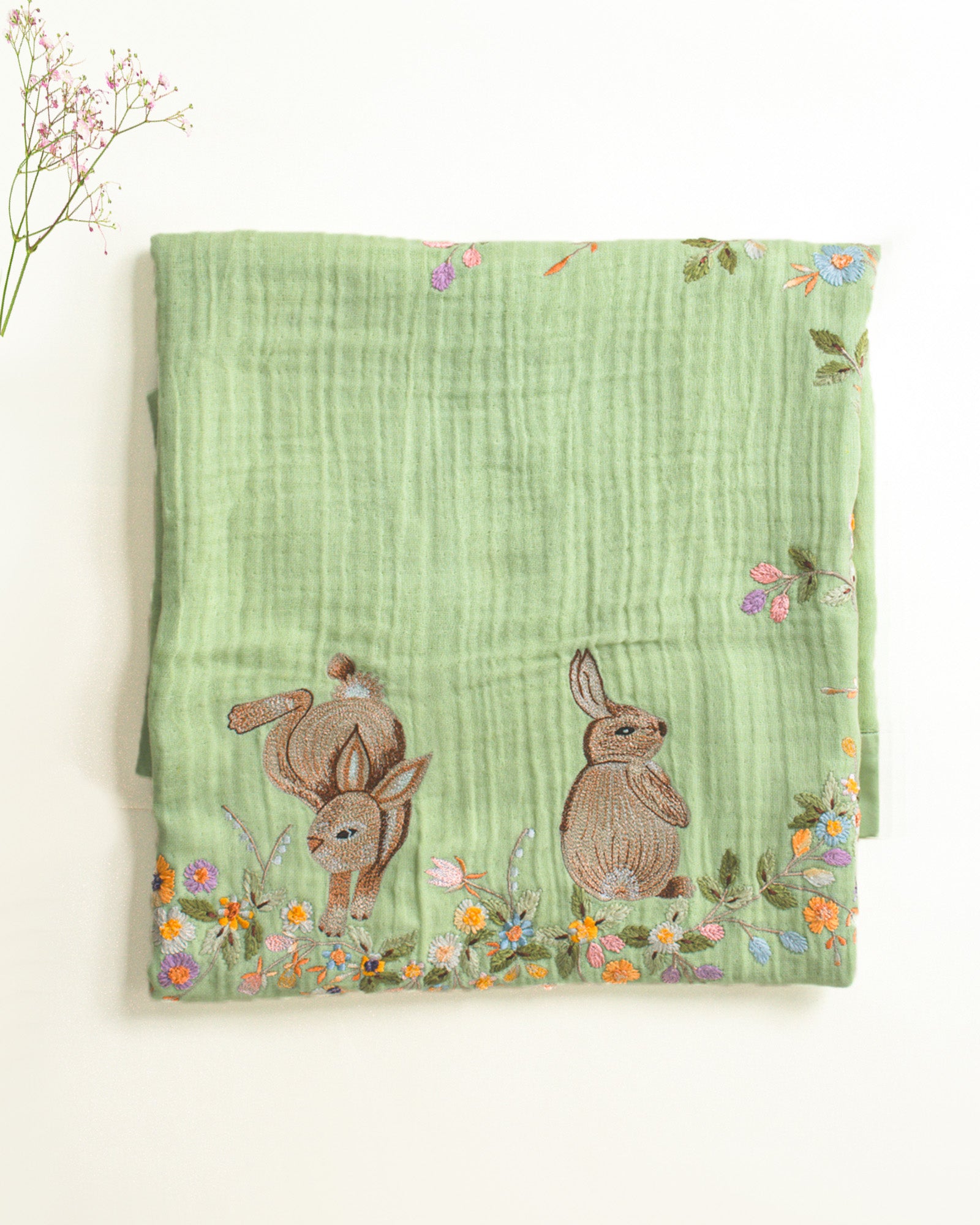 Soft green baby dohar with delicate embroidery featuring two bunnies surrounded by a floral wreath. Made from lightweight, breathable fabric with a satin border—perfect for cozy naps and gentle on baby’s skin.