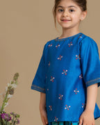 A young girl wearing  Laad`s  vibrant blue embroidered kurta with delicate floral motifs, paired with checkered blue and green patiala pants and a matching dupatta with gold detailing. 