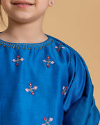 A young girl wearing  Laad`s  vibrant blue embroidered kurta with delicate floral motifs, paired with checkered blue and green patiala pants and a matching dupatta with gold detailing. 