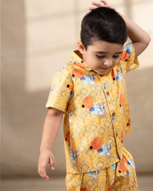 A cheerful Laad`s co-ord set in a vibrant yellow hue, featuring playful deer and geometric prints, a collared button-down shirt, and matching shorts.