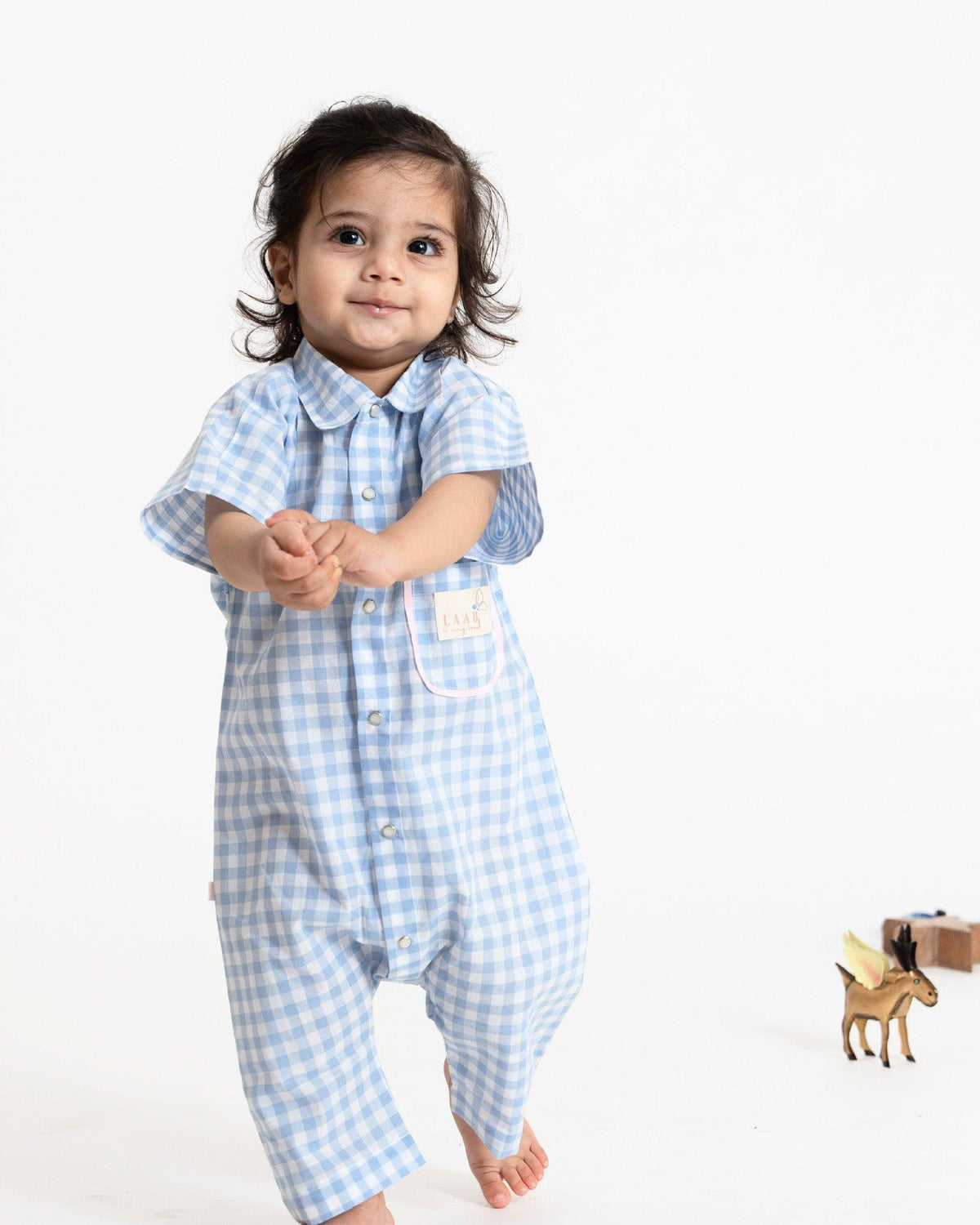 A stylish blue-and-white gingham romper featuring a collared neckline for a polished look. Designed with a front snap-button closure for easy dressing and a patch pocket with fine detailing for a playful touch perfect kidswear.