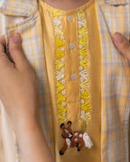laad`s kid wearing a pastel yellow kurta with embroidered reindeer details, paired with a checkered Nehru jacket and white trousers,