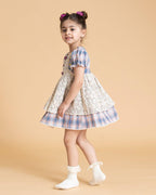 Laad`s kid in tea dress by Laad India, featuring delicate floral embroidery, plaid puff sleeves, and a charming layered design. Made with soft, breathable fabric, perfect for festive occasions and everyday elegance."
