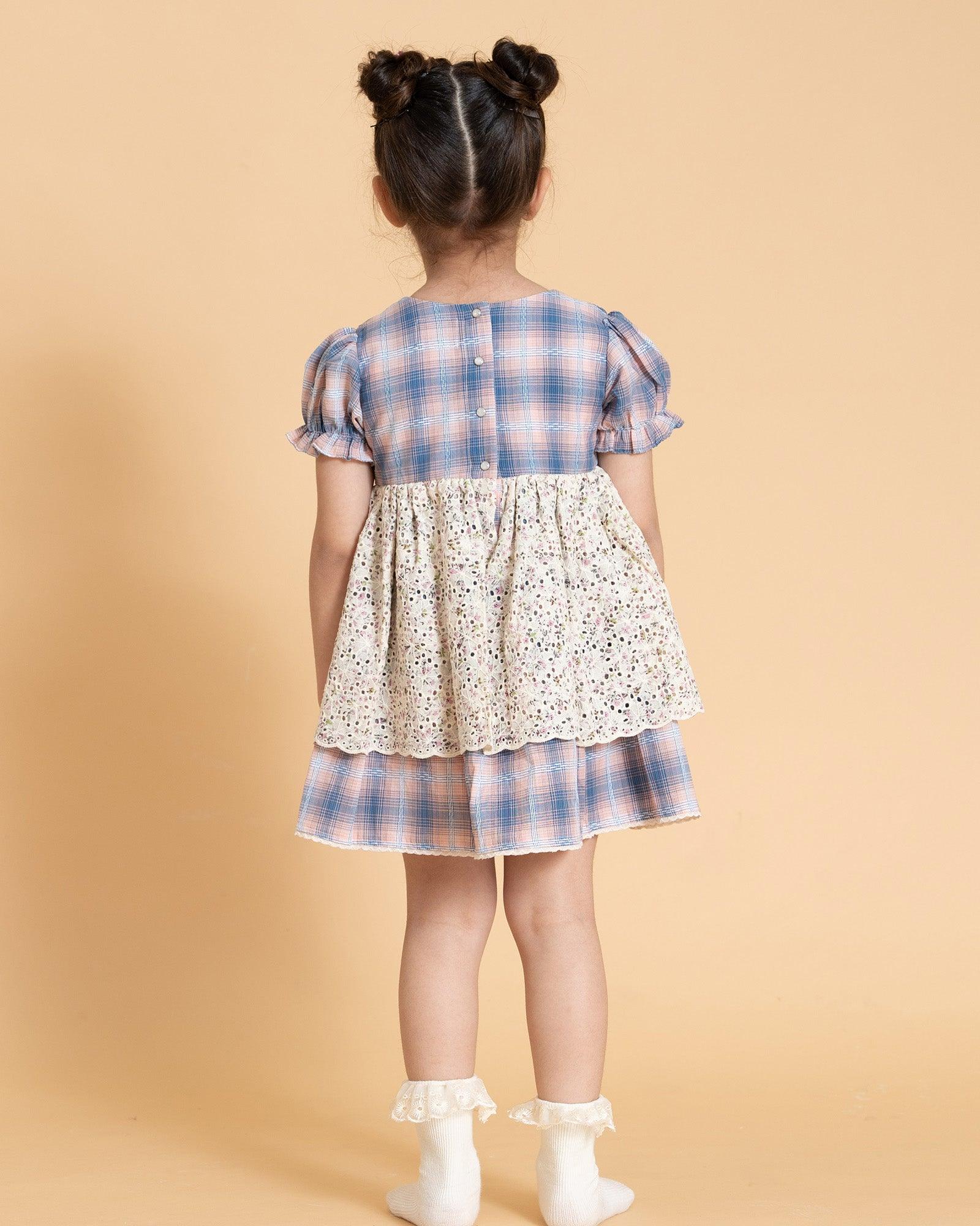 laad`s kid in tea dress by Laad India, featuring delicate floral embroidery, plaid puff sleeves, and a charming layered design. Made with soft, breathable fabric, perfect for festive occasions and everyday elegance."