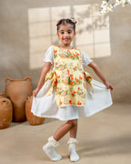 LAAD`S Girl in floral apron dress with a bunny and tulip print, layered over a white puff-sleeve dress. Features ruffled side panels and delicate lace trim. Soft, breathable fabric for comfort and charm.