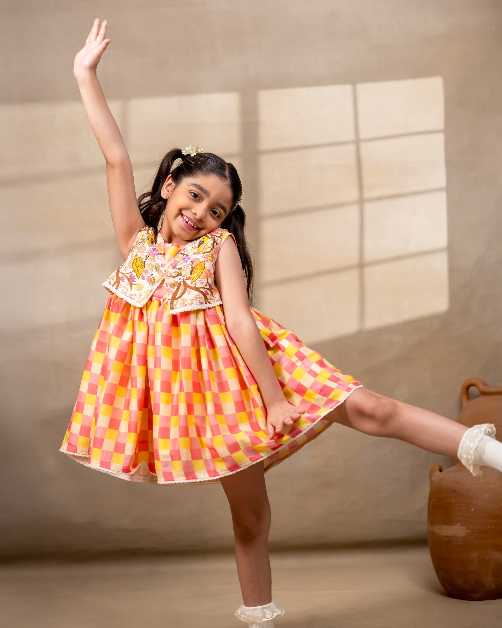 laad girl wearing a sleeveless zinnia dress set with with pink and yellow checkered print  and embroidered jacket 