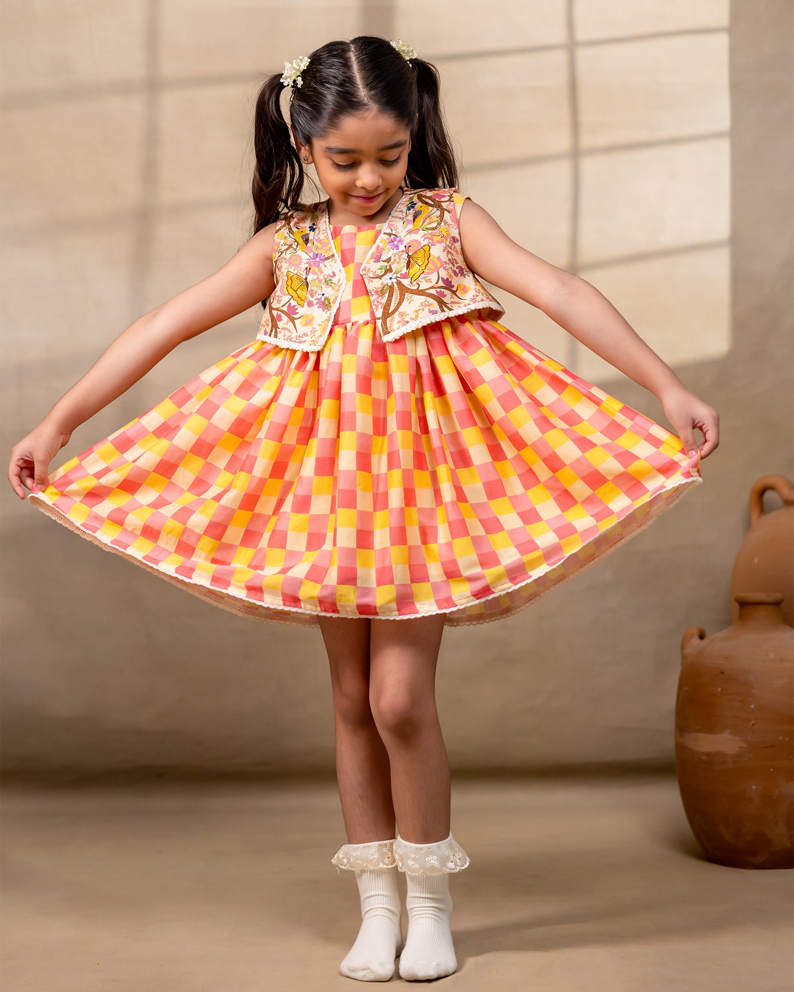 laad girl wearing a sleeveless zinnia dress set with with pink and yellow checkered print  and embroidered jacket 