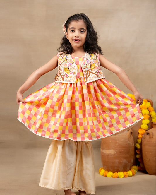 Girl wearing the Zinnia Sharara Set, featuring a vibrant checkered kurta with embroidered and printed jacket detailing along with flared and golden sharara pants, perfect for festive occasions.