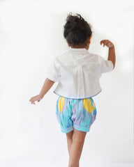 baby girl wearing  Laad`s gwhite cropped shirt with scalloped trim and hand-embroidered button on it along with pastel aqua bubble shots featuring a pleated abstract design.