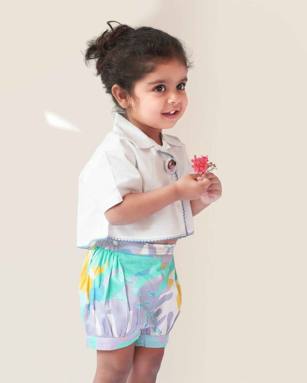 baby girl wearing  Laad`s gwhite cropped shirt with scalloped trim and hand-embroidered button on it along with pastel aqua bubble shots featuring a pleated abstract design.