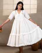 Woman wearing laad`s  white cotton midi dress with floral embroidery, scalloped neckline, and ruffled hem