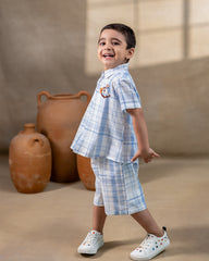 LAAD`S kids in co-ord set featuring a light blue and white plaid short-sleeve button-up shirt with matching shorts. The shirt is adorned with delicate embroidery of a rocking horse on the chest,
