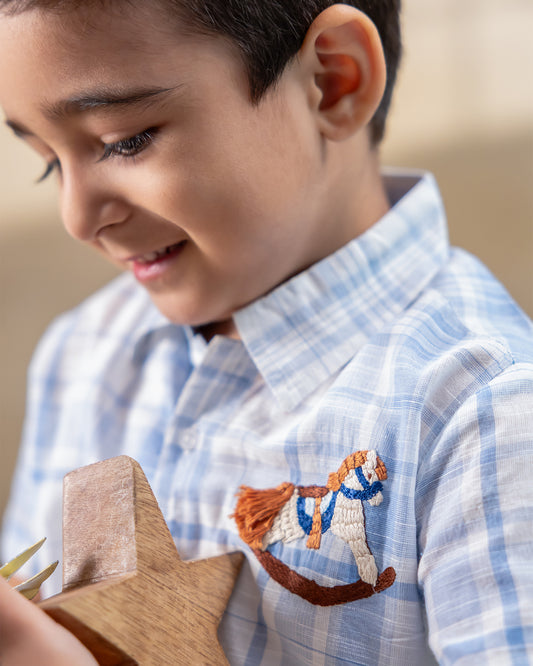 LAAD`S kids in co-ord set featuring a light blue and white plaid short-sleeve button-up shirt with matching shorts. The shirt is adorned with delicate embroidery of a rocking horse on the chest,