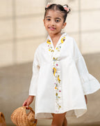 Little girl in a white hand-embroidered A-line girls party dress with flared sleeves and colorful bird and floral detailing, holding a wicker basket.