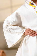 Little girl in a white hand-embroidered A-line girls party dress with flared sleeves and colorful bird and floral detailing, holding a wicker basket.