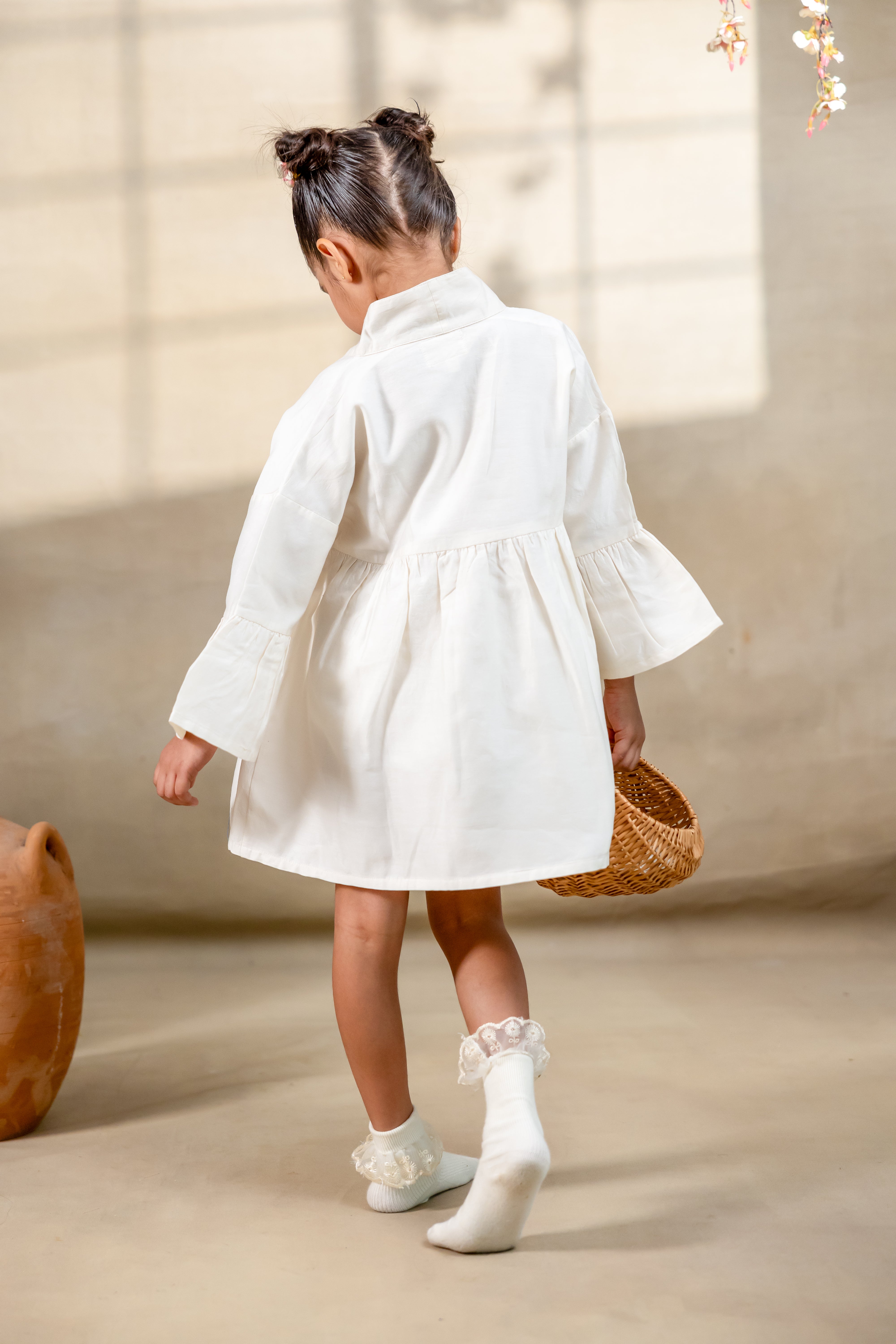 Little girl in a white hand-embroidered A-line dress with flared sleeves and colorful bird and floral detailing, holding a wicker basket.