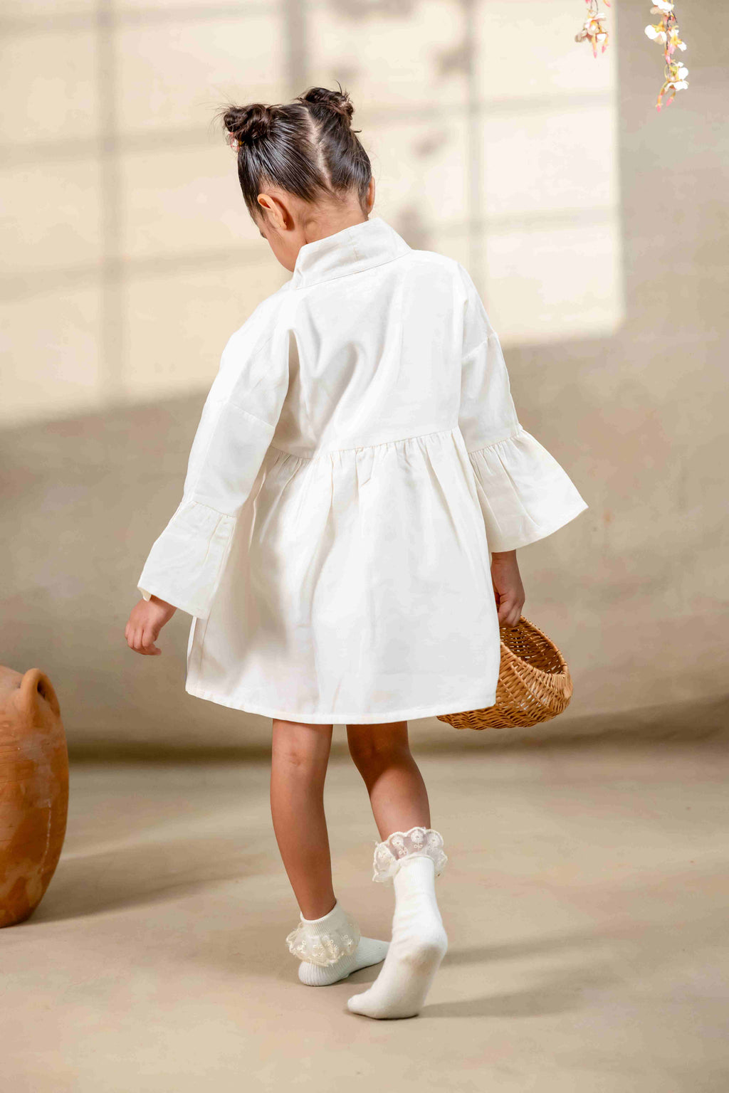 Little girl in a white hand-embroidered A-line girls party dress with flared sleeves and colorful bird and floral detailing, holding a wicker basket.