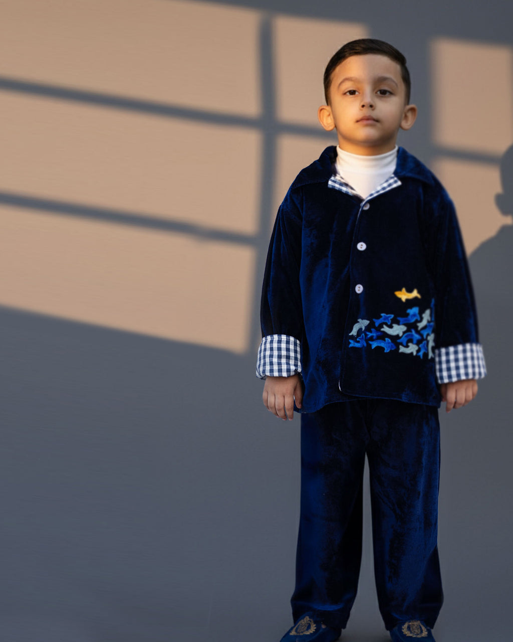 Midnite Shoal co-ord set by LAADINDIA.com, featuring a child dressed in a navy blue velvet co-ord with floating fish embroidery, front-open top with contrast check cuffs, and matching trousers for winter festive wear.