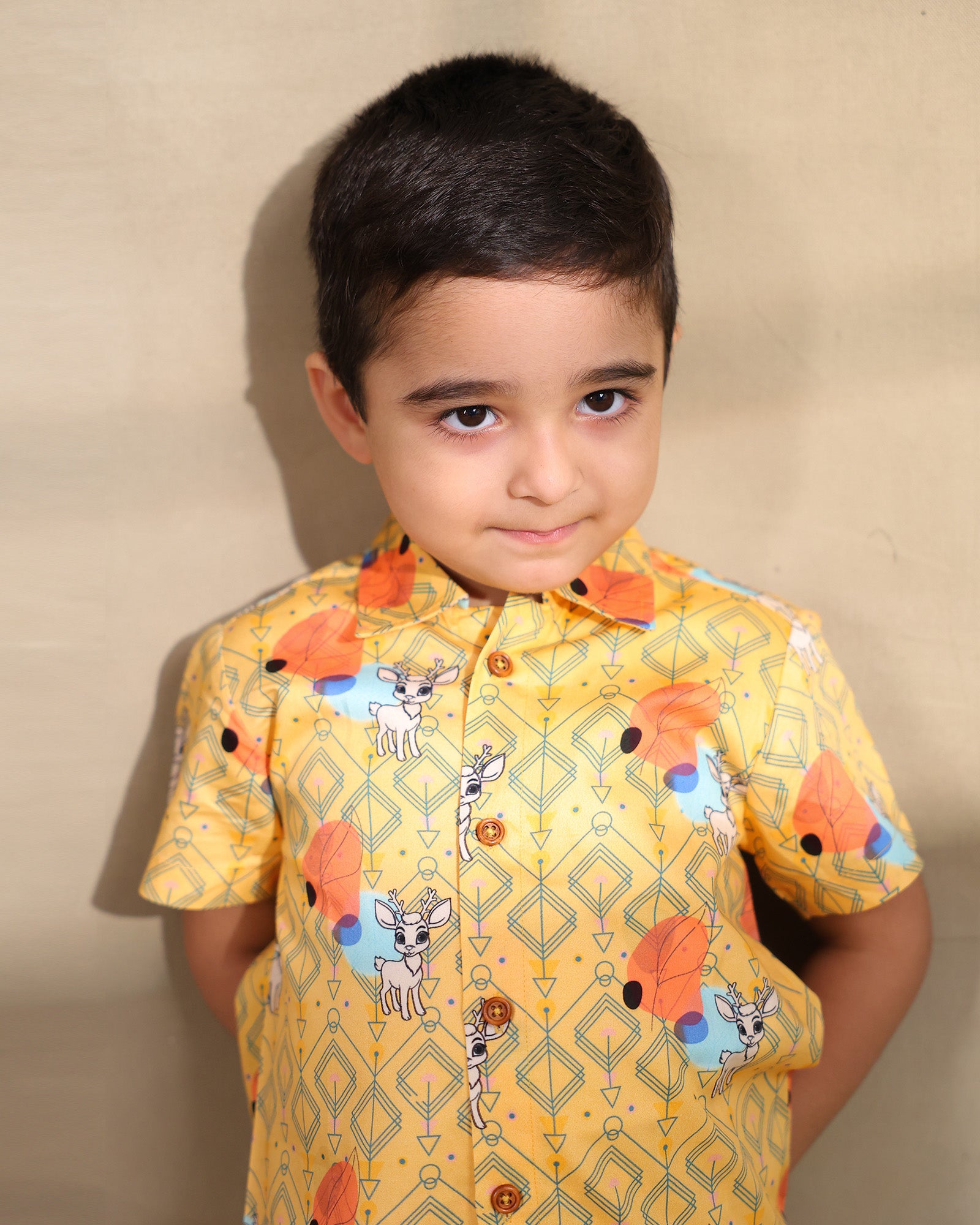 A cheerful Laad`s co-ord set in a vibrant yellow hue, featuring playful deer and geometric prints, a collared button-down shirt, and matching shorts.