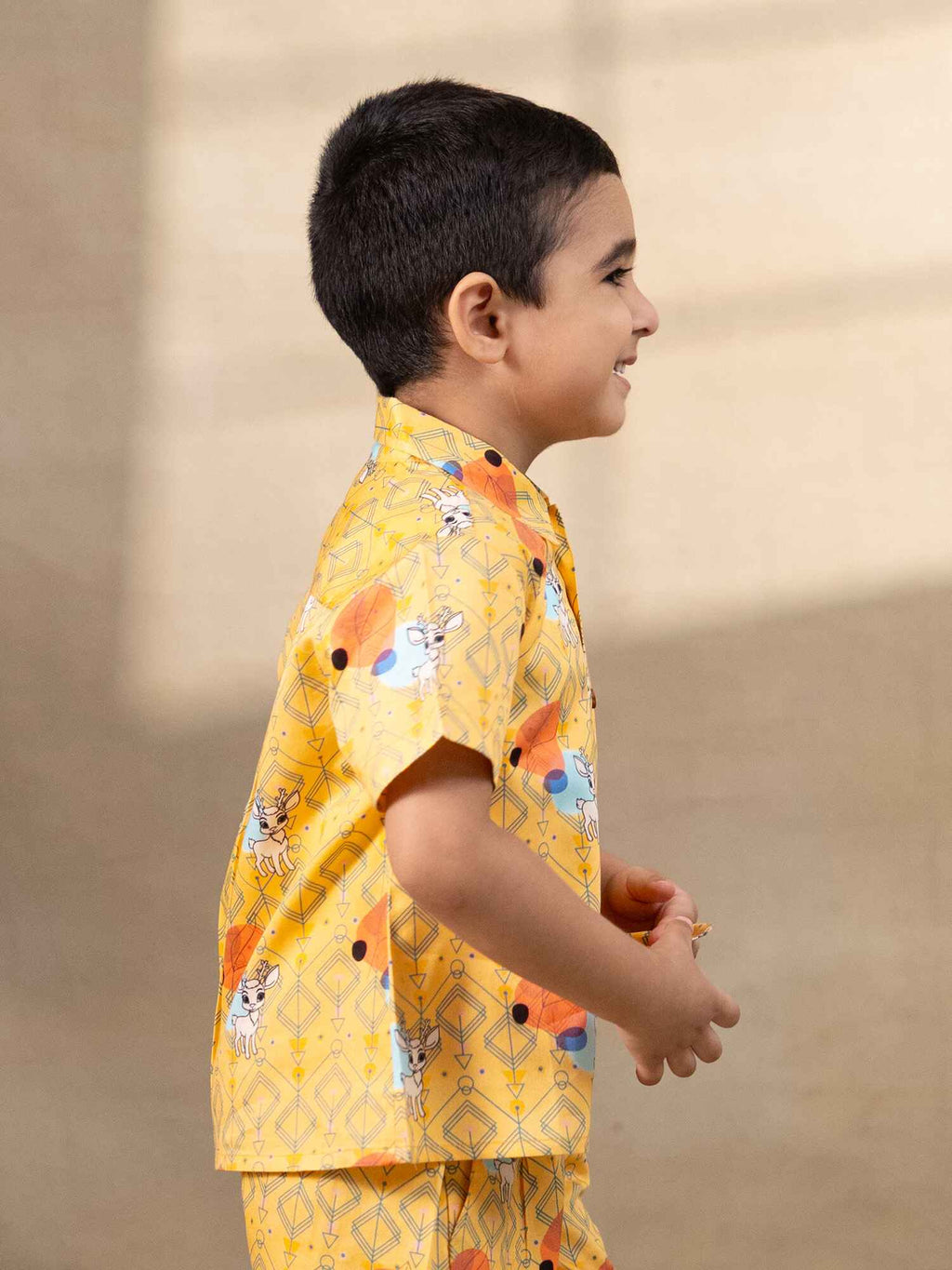 A cheerful boy`s Laad`s co-ord set boy`s shirt and shorts in a vibrant yellow hue, featuring playful deer and geometric prints, a collared button-down shirt, and matching shorts.
