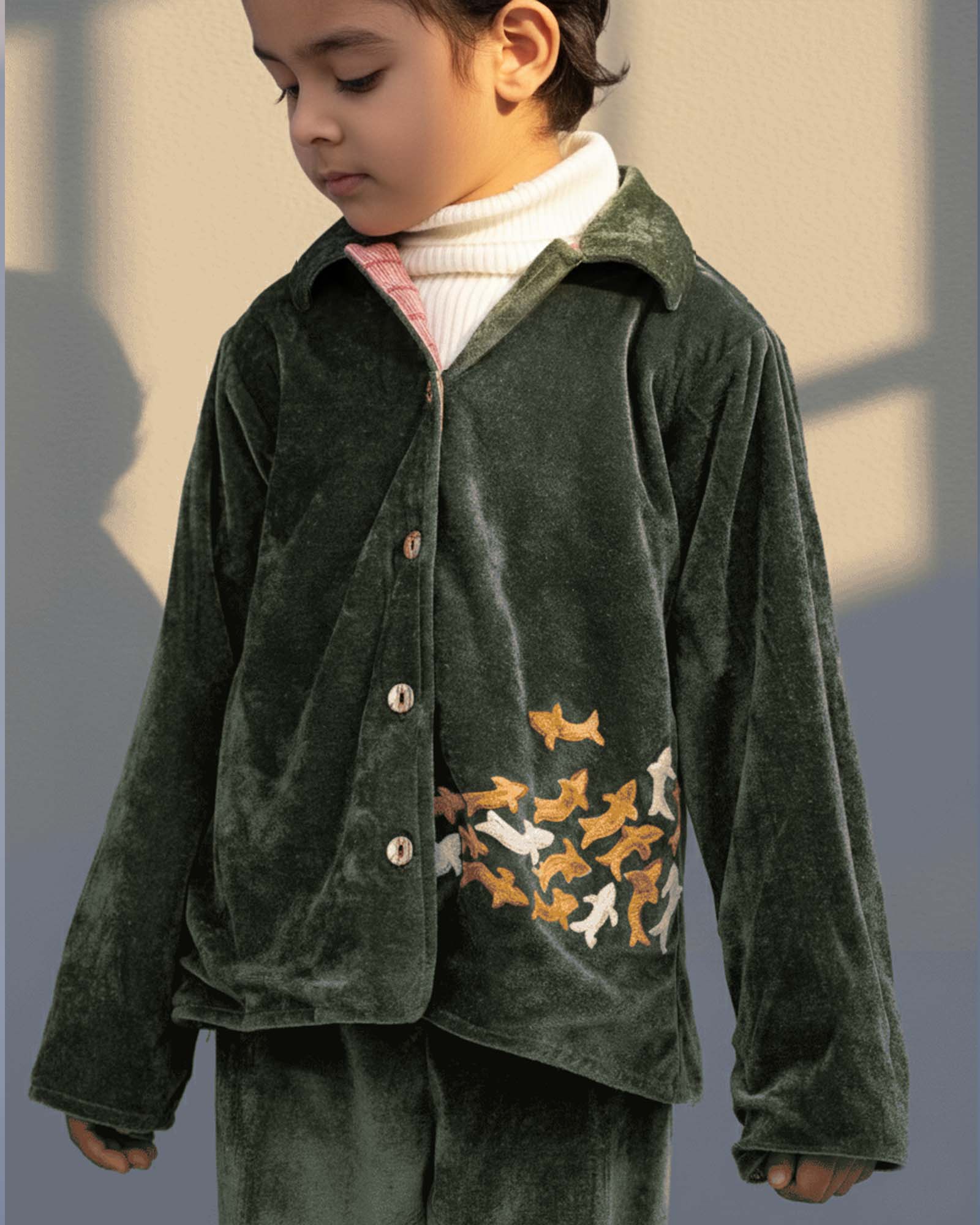 sage shoal co-ord set by LAADINDIA.com, featuring a child dressed in a navy blue velvet co-ord with floating fish embroidery, front-open top with contrast check cuffs, and matching trousers for winter festive wear.