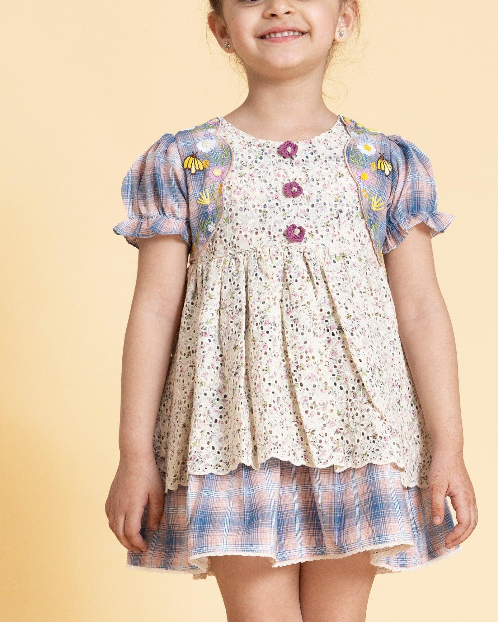 laad`s kid in tea dress by Laad India, featuring delicate floral embroidery, plaid puff sleeves, and a charming layered design. Made with soft, breathable fabric, perfect for festive occasions and everyday elegance."