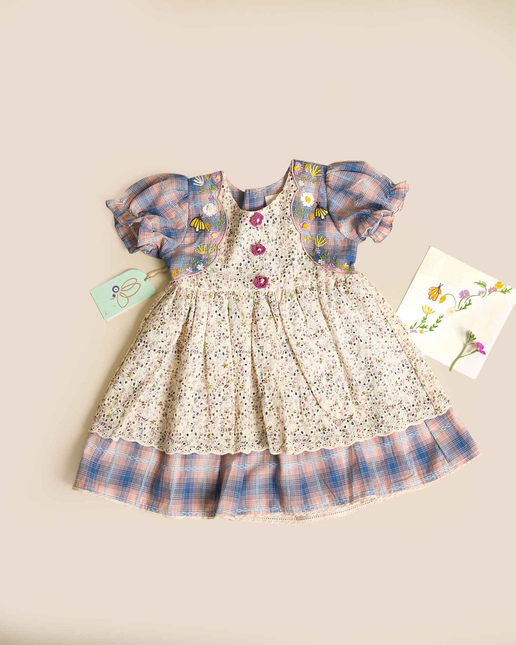 Laad`s kid in tea dress by Laad India, featuring delicate floral embroidery, plaid puff sleeves, and a charming layered design. Made with soft, breathable fabric, perfect for festive occasions and everyday elegance."