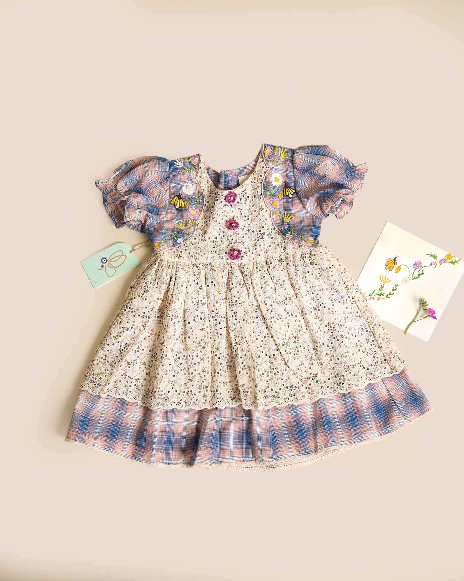 Laad`s kid in tea dress by Laad India, featuring delicate floral embroidery, plaid puff sleeves, and a charming layered design. Made with soft, breathable fabric, perfect for festive occasions and everyday elegance."