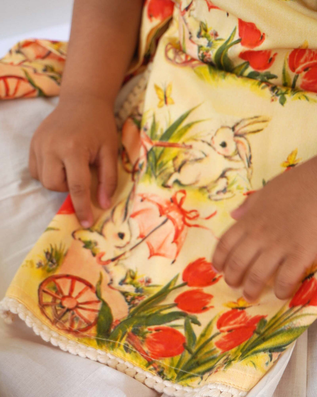 LAAD`S Girl in floral apron dress with a bunny and tulip print, layered over a white puff-sleeve dress. Features ruffled side panels and delicate lace trim. Soft, breathable fabric for comfort and charm.