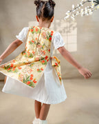 LAAD`S Girl in floral apron dress with a bunny and tulip print, layered over a white puff-sleeve dress. Features ruffled side panels and delicate lace trim. Soft, breathable fabric for comfort and charm.