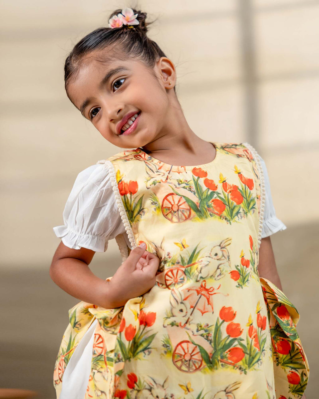 LAAD`S Girl in floral apron dress with a bunny and tulip print, layered over a white puff-sleeve dress. Features ruffled side panels and delicate lace trim. Soft, breathable fabric for comfort and charm.