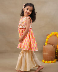 Girl wearing the Zinnia Sharara Set, featuring a vibrant checkered kurta with embroidered and printed jacket detailing along with flared and golden sharara pants, perfect for festive occasions.